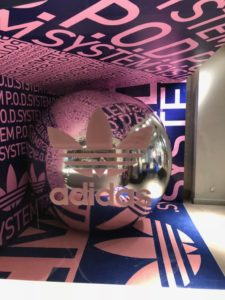 Adidas retail display featuring a large chrome sphere with the Adidas logo, surrounded by large format print graphics on walls and floor.