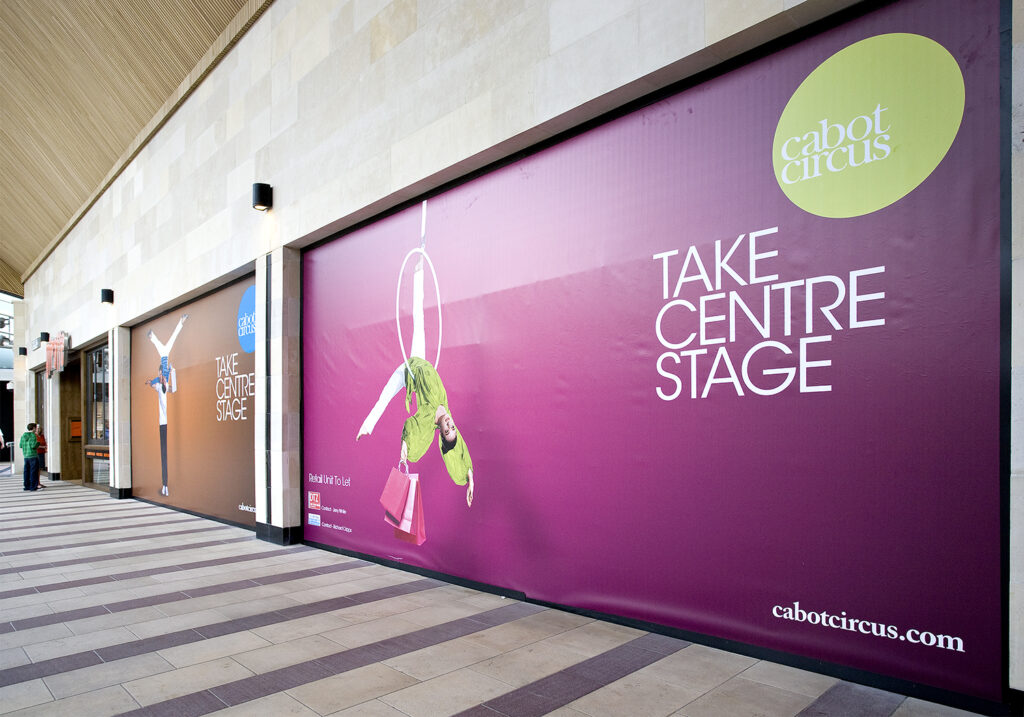 Retail window graphics for Cabot Circus, showing acrobatic figures and "TAKE CENTRE STAGE" on a purple panel.