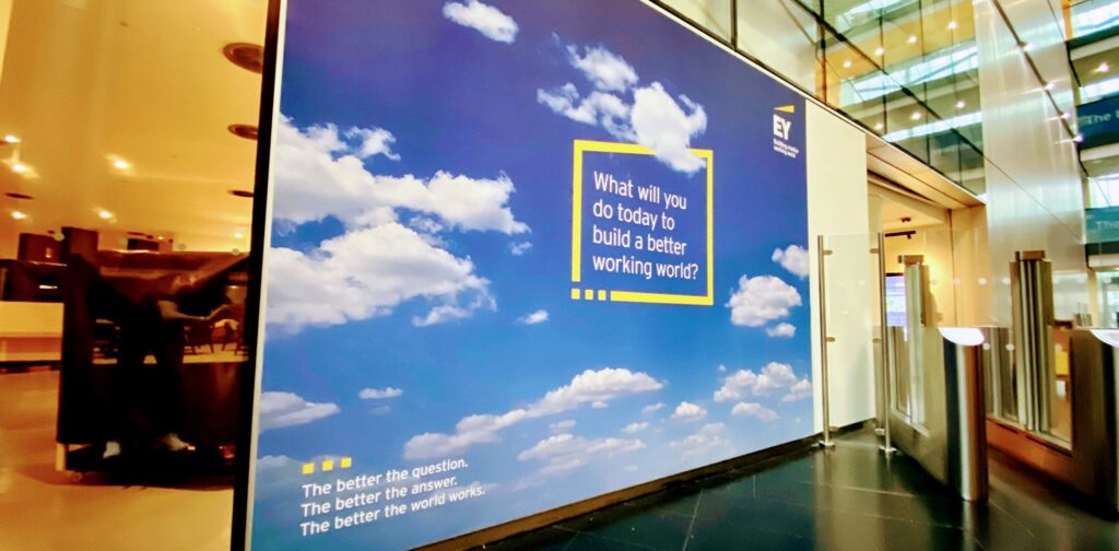 Large EY corporate wall graphic with blue sky and motivational text in an office lobby