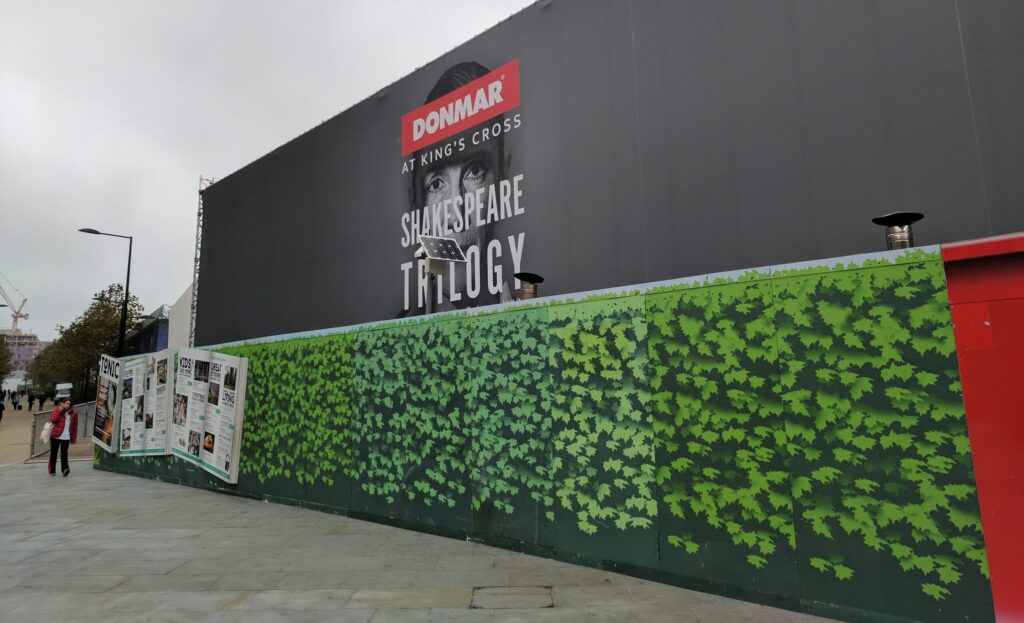 Construction hoarding with a large format print advertisement for Donmar at King's Cross and a green foliage design.