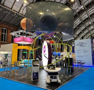 A futuristic, space-themed exhibition booth with a large cylindrical screen showing planets, glowing lights, and high-top tables.