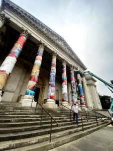 outdoor signage material, classical building with a grand staircase and columns wrapped in colourful, banknote-like collages