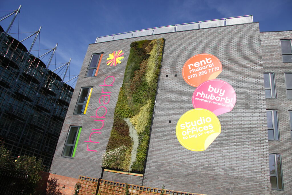 Office and corporate signage on a grey brick building with a vertical living wall and colourful "rhubarb" branding.