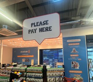 POS signage at an ebebek store with a large speech bubble sign that says "PLEASE PAY HERE."
