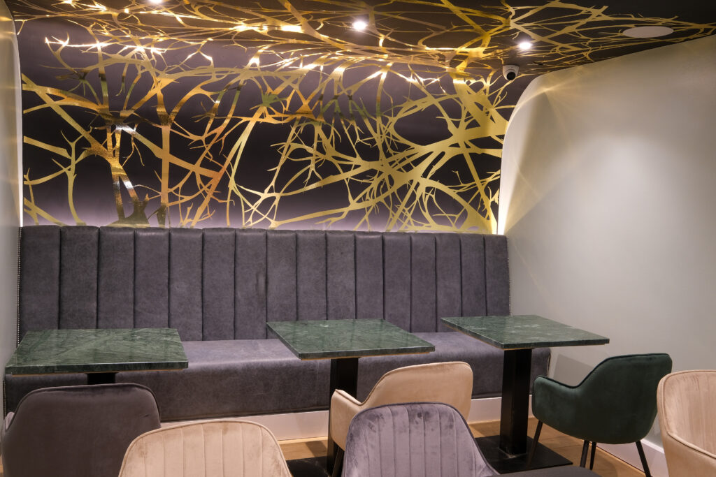 Modern restaurant interior at West One with gold branch-patterned ceiling.