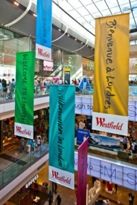 Westfield shopping centre interior with multiple welcome banners hanging from the ceiling in different languages.