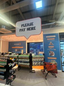 Interior of an Ebebek baby store. A large 'PLEASE PAY HERE' sign hangs above a checkout counter with an orange shopping cart in front.