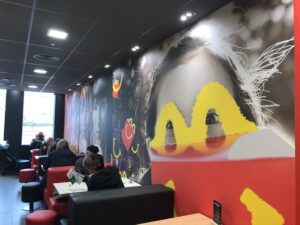 The interior of a McDonald's restaurant with a large mural of a person's face and a yellow M logo painted over their eyes.