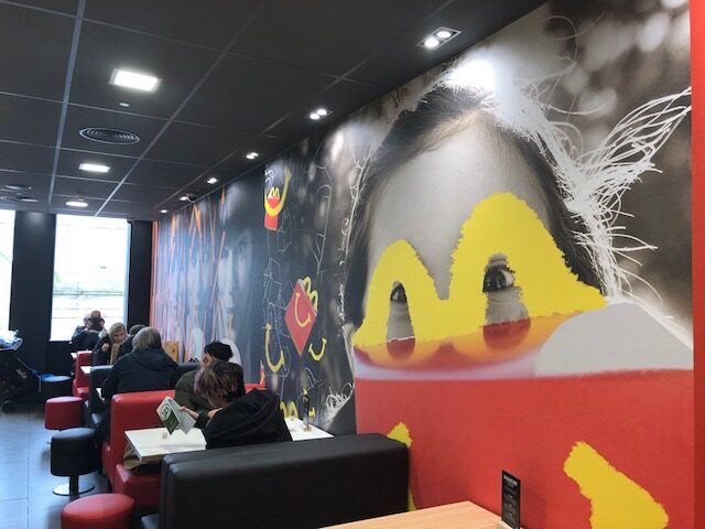 The interior of a McDonald's restaurant with a large mural of a person's face and a yellow M logo painted over their eyes.
