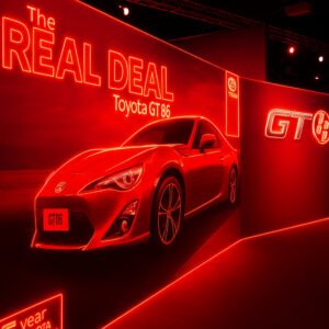 Indoor promotional display for the Toyota GT86 sports car, illuminated entirely in bright red light, featuring the car and neon text reading 'The REAL DEAL'.
