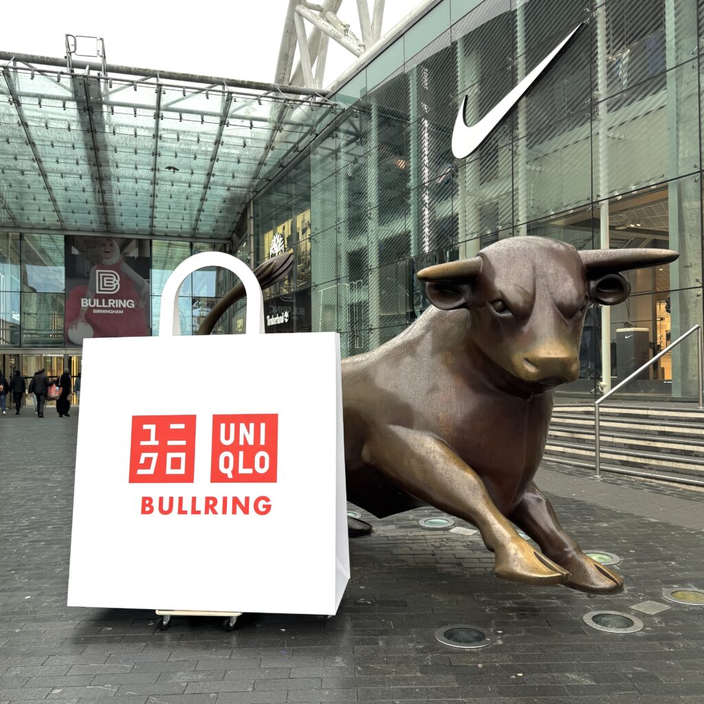 Uniqlo - tension fabric display of a bag with the uniqlo logo and bullring written on it infront of the bronze birmingham bull in front of the bullring shopping centre.