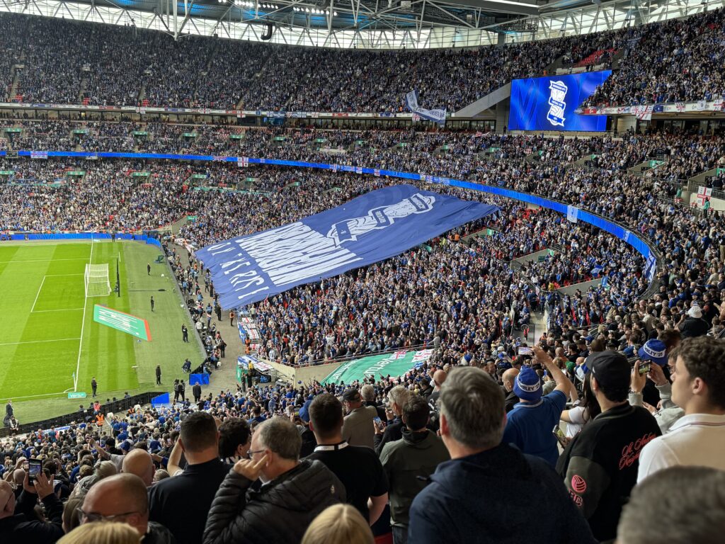 Large Tifo in a football stadium signs in front of a large crowd, with the birmingham city football club logo on it