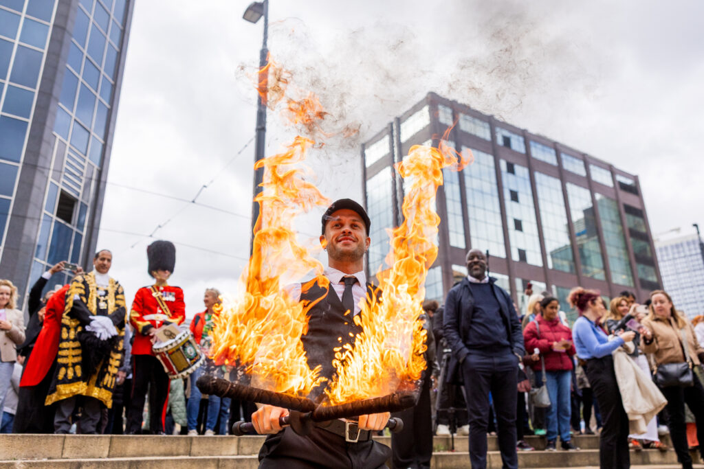 a man with two stick on fire, dressed in a suit and a flat cap with the lord mayor and a beefeater behind him at the international day of Birmingham